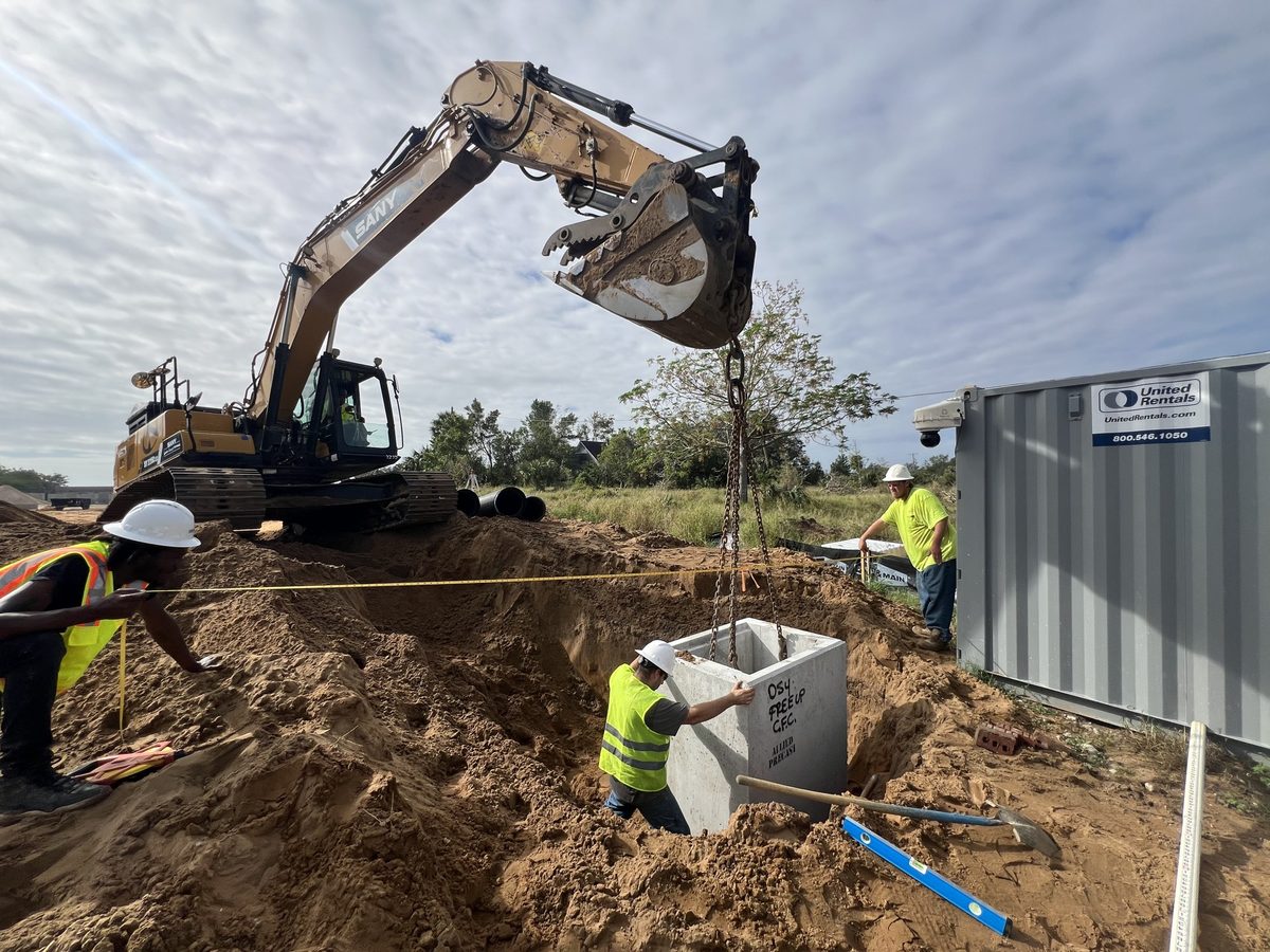 Central Florida Civil crew setting a precast drainage structure with an excavator