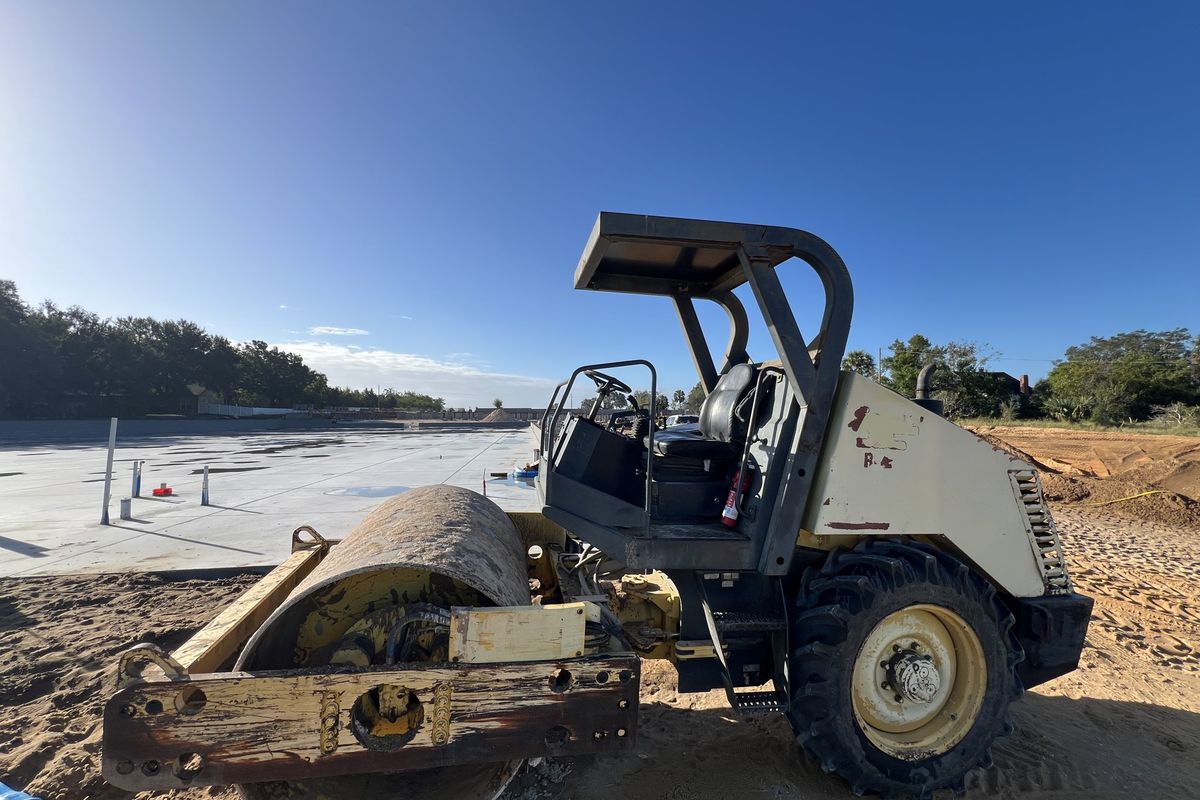 Smooth drum roller compacting subgrade next to a lined pond