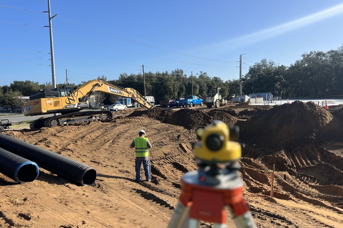 Surveyor shooting grades with HDPE storm pipe staged on site