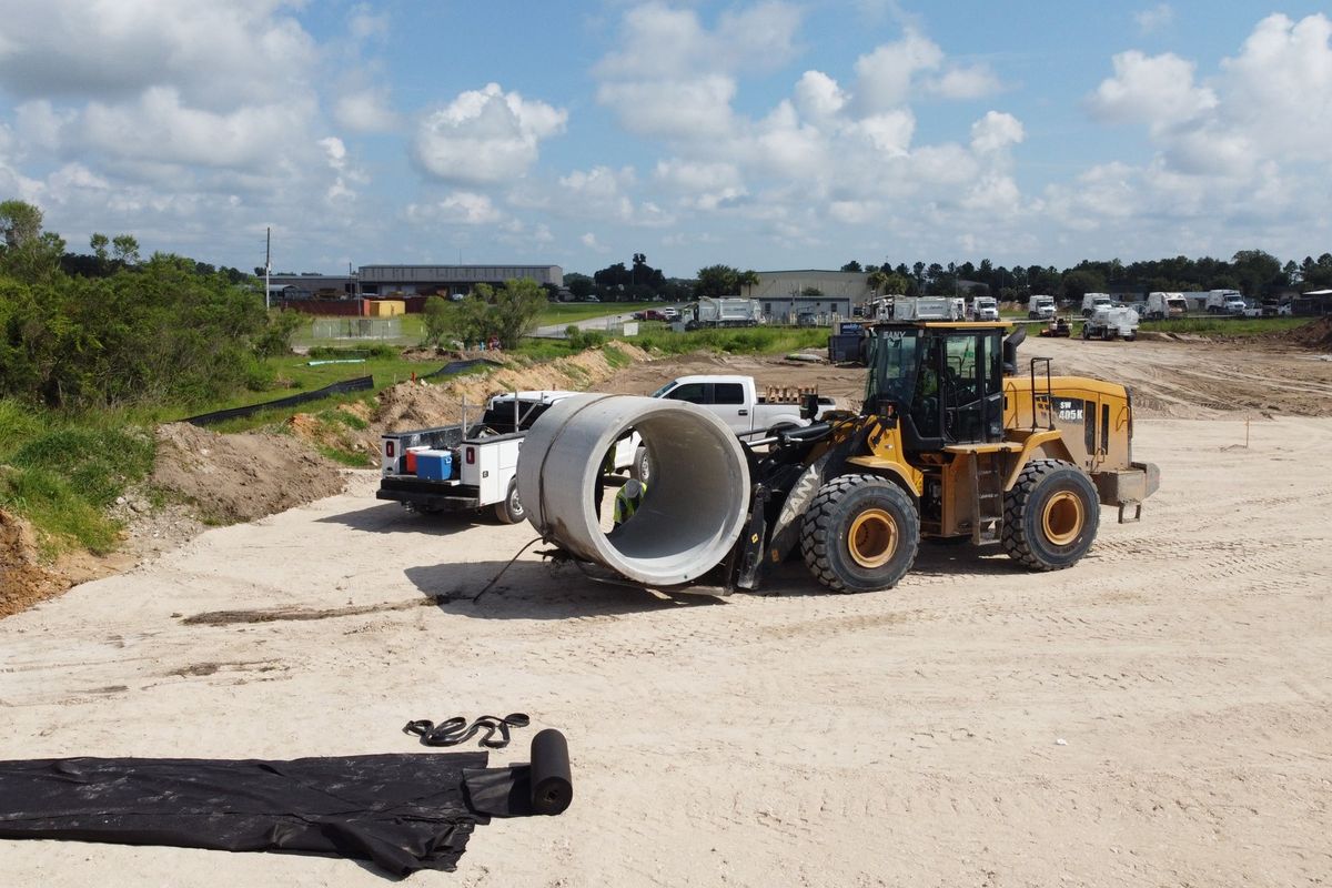 Wheel loader carrying a large reinforced concrete pipe across a job site